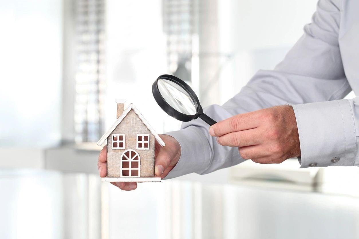 A person holding a small house and magnifying glass