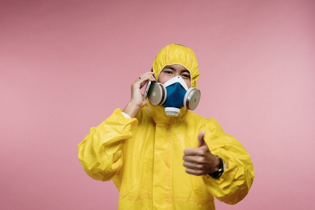 A man in yellow and white hazmat suit holding up two cans.